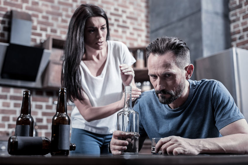 Alcoholic in a family. Brutal bearded sad man sitting in front of the vodka bottle and thinking about his problems while drinking at home