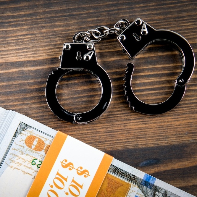A pair of handcuffs and a stack of bills are on a wooden table.